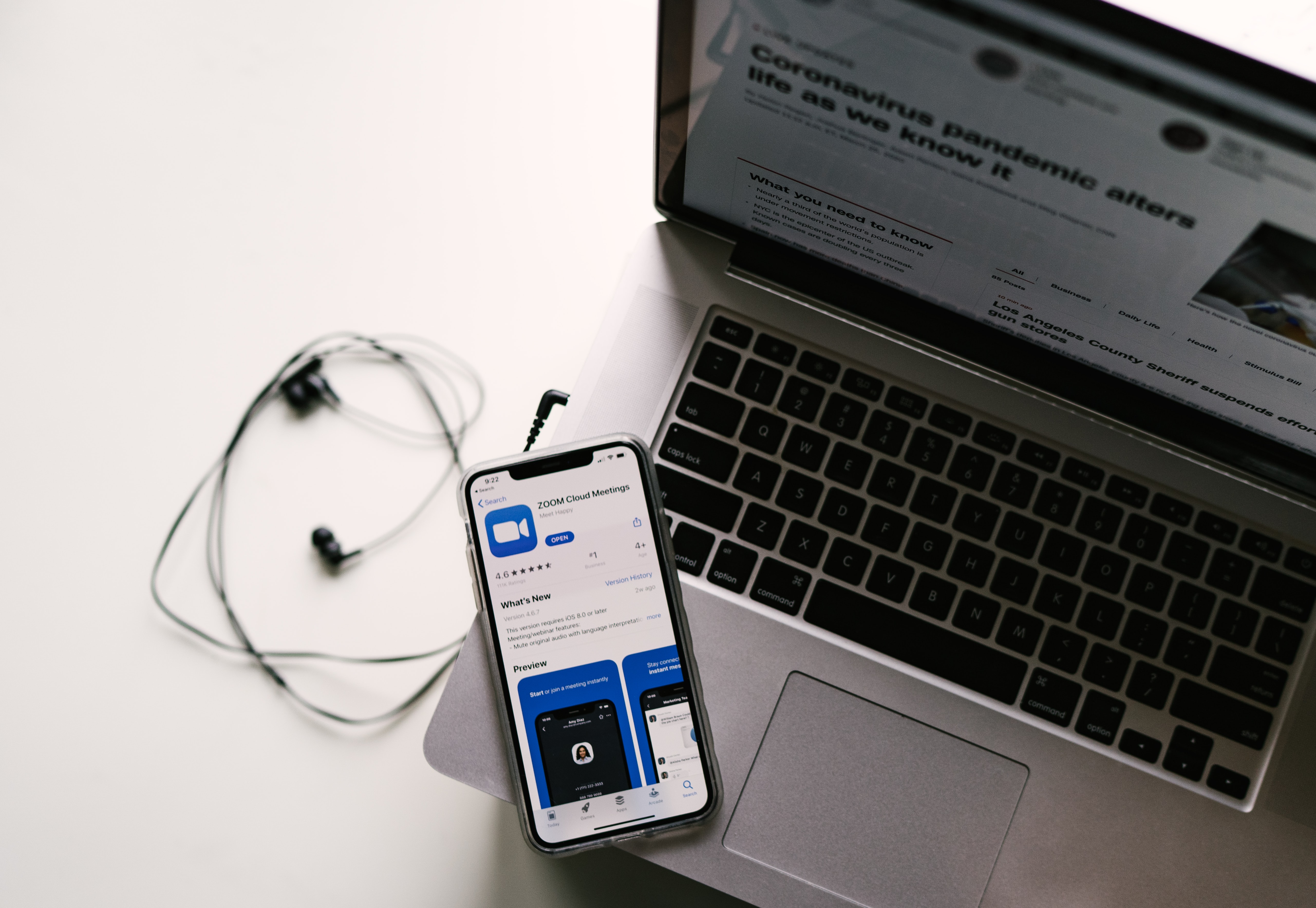 A phone displaying Zoom in an app store, resting on a laptop with a coronavirus-related news story. C: Allie Smith, Unsplash