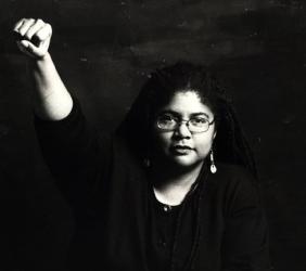 A photo of Linda Thurston, a Black woman with dreadlocks, her right fist raised